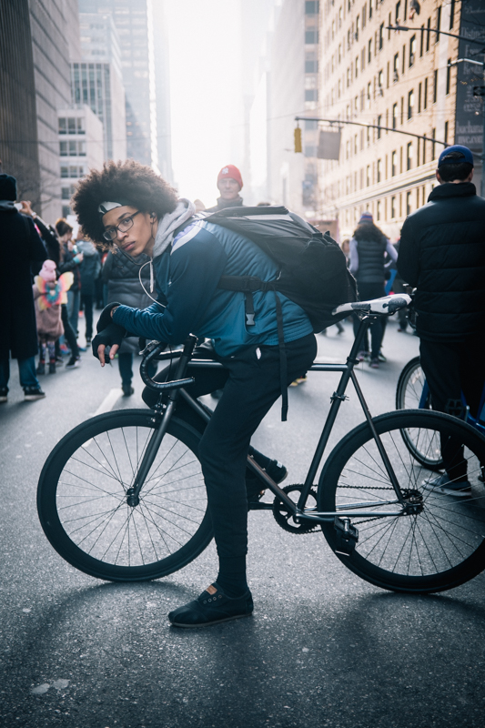 rides an unbranded fixed gear bike  photographed at 3rd Ave. and 48th St.,  Manhattan during the Women's March NYC (attempting to make a delivery) 